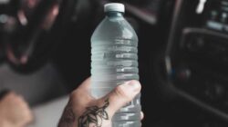 A tattooed hand holds a plastic water bottle.